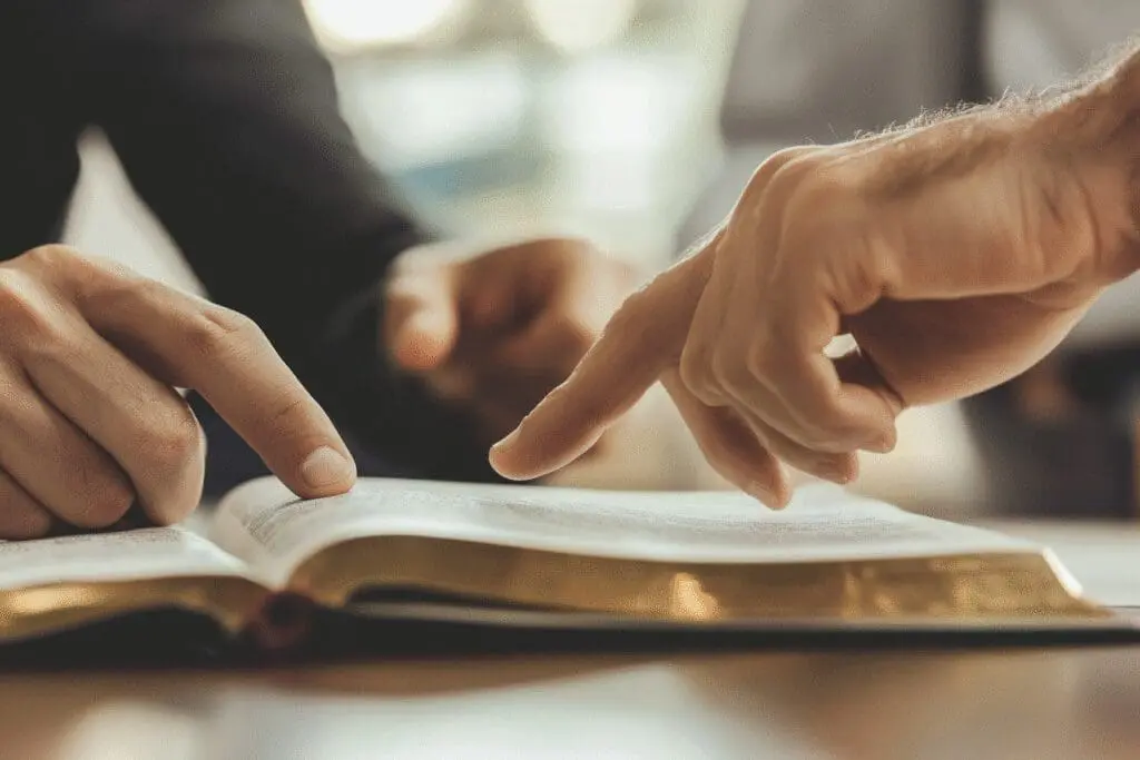 A close-up of a mentor's hands pointing to a passage in the Bible, giving expert advice to a student