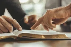 A close-up of a mentor's hands pointing to a passage in the Bible, giving expert advice to a student