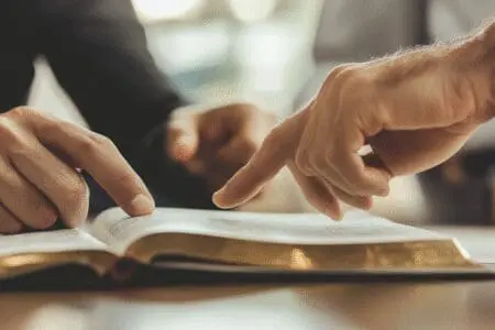 A close-up of a mentor's hands pointing to a passage in the Bible, giving expert advice to a student