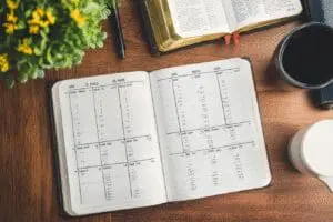 A wall calendar with checkmarks and an open Bible on a desk, illustrating a successful plan to read the Bible in a year.