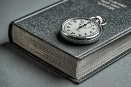 A stopwatch placed beside a Bible representing the answer to how many hours to read the Bible