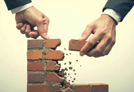 a hand removing a foundational block from a wall symbolizing the destabilizing nature of stealing